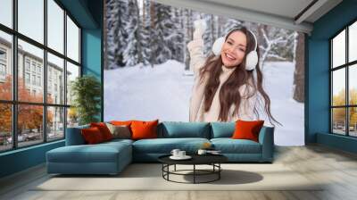 Young pretty happy woman in white coat and fur headphones walking in snowy forest, having fun and playing snowballs Wall mural