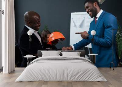 A male African American engineer with a construction helmet in his hands shakes hands with a business partner or investor Wall mural