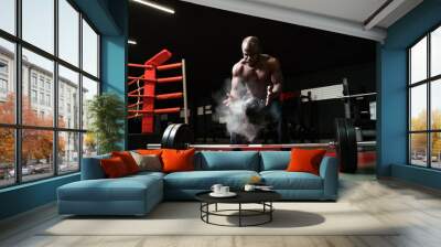 An African American man sprays magnesium or talcum powder with his palms before lifting a barbell. Heavyweight preparing for competition Wall mural