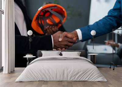 Close-up of a handshake of two African American men. An investor hands over an orange construction helmet to a developer. Building permit Wall mural