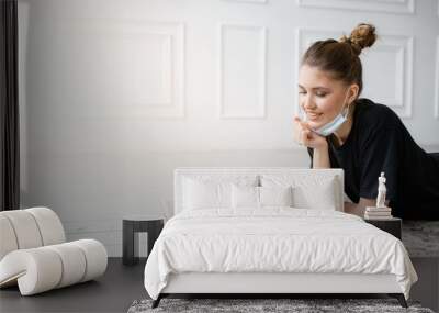 Girl lying on carpet at home with a laptop by removing the mask on the face home hair in the mode of self-isolation Wall mural