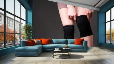 Photo of female hands. The girl pulls a black knee pad on her leg. Isolated on dark background Wall mural