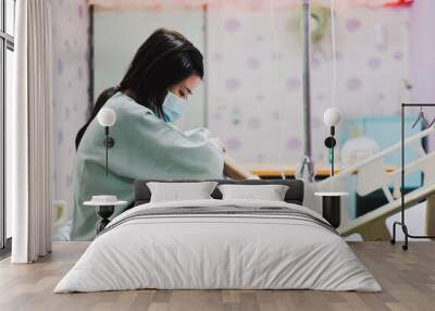 Asian sick woman with blue mask and hospital uniform sit on bed and sad mood Wall mural