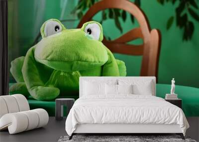 A plush frog sitting on the table with a green cloth, cover Wall mural