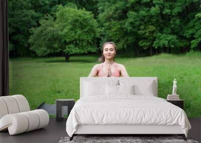 Beautiful Asian yogi woman practicing yoga in the park holding her palms together sitting on yoga mat. Early morning meditation with closed eyes. Wall mural