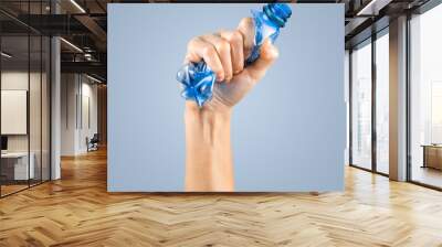 female hand squeezes an empty plastic bottle isolated on the blue. waste recycling concept Wall mural