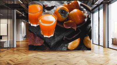 Ripe orange persimmon fruit and persimmon leaves in a brown plate on a black wooden table Wall mural