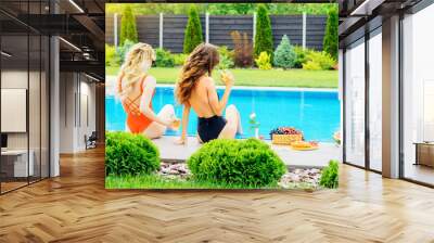 Two beautiful girls in swimsuits drinking cocktails and relaxing near the pool. Summer vacation and pooltime. Wall mural