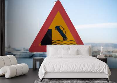 Triangular warning road sign, yellow with red outline depicting a car falling off a harbor dock. Drive carefully, pier embankment Wall mural