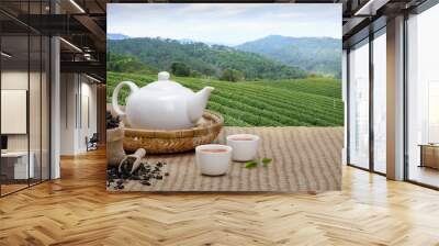 Warm cup of tea with teapot, green tea leaves and dried herbs on the bamboo mat at morning in plantations background with empty space, Organic product from the nature for healthy with traditional Wall mural