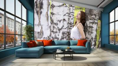 A girl with long hair is standing by the white trunks of a birch Wall mural