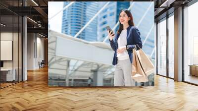 Asian business woman standing at outdoor with shopping bags city building background with blue sky spending money lifestyles Wall mural