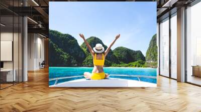 Rear view of young adult traveling tourist woman hand raised sitting on the sailing boat on summer vacation southeast asia trip Wall mural