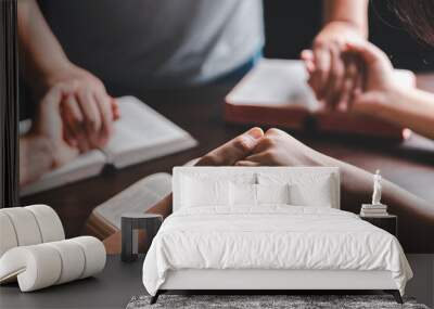 Christian group praying for globe and people around the world on wooden table with bible. Christian small group holding hands and praying together around a wooden table with bible page in homeroom. Wall mural