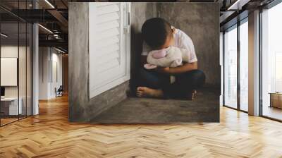 Dramatic portrait of little boy sitting on floor and cuddling teddy bear Wall mural