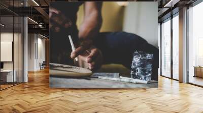 Hand holding cigarette mixed with marijuana closeup on chopping board background Wall mural