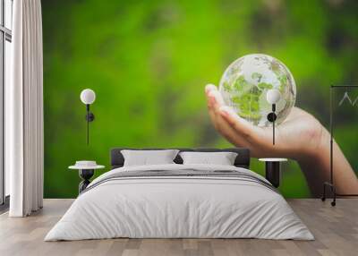 Human hands holding earth sphere crystal or sustainable globe glass with sunlight at green nature background in ecology environment forest. concept of conservation environmental, protection planet. Wall mural