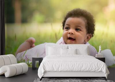 Cute little dark skinned baby boy smiling with happiness while lying on the grass in the park. Wall mural