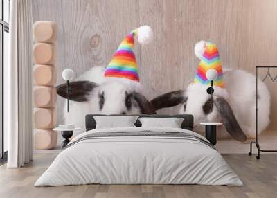 Two cute white and black Easter bunny rabbit wearing colorful party hat sitting on grey wooden surface and background with 6 wooden cube block stack on each other. Easter holidays party concept. Wall mural