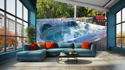 A large aqua blue colored empty hot tub on a patio deck next to a red BBQ. The water in the tub has steam rising from the clear water with bubbles. There are lush green trees in the background. Wall mural