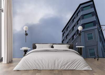 An upward partial view of a tall concrete building with lots of double hung windows.  A grey cloudy sky is the background to the condo building. The textured exterior walls are of two  tones of grey.  Wall mural