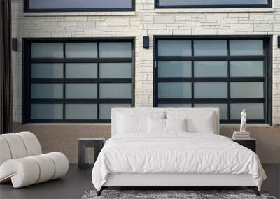 The exterior of a grey brick wall of a modern luxury house with two new glass garage doors. The trim around the doors is black metal. There are multiple panes. The driveway is tan colored concrete.  Wall mural