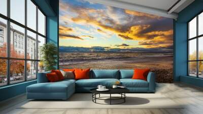 A view of a stony beach at sunset with crashing waves and ecume under a majestic yellow cloudy stormy sky Wall mural