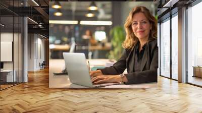 Friendly older woman smiling at camera, working on a laptop  Wall mural