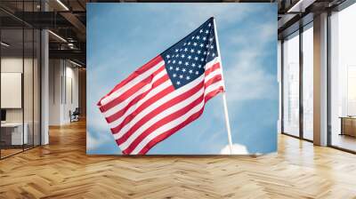 An American flag fluttering in the wind against a blue sky with clouds. Wall mural