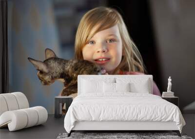 Portrait of a smiling girl with a Cornish rex cat in her arms. Wall mural