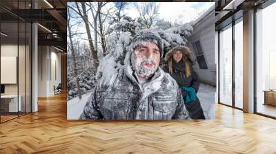 Two Yong Women In Winter Coats Playfully Push A Young Mans Face Into The Snow Wall mural