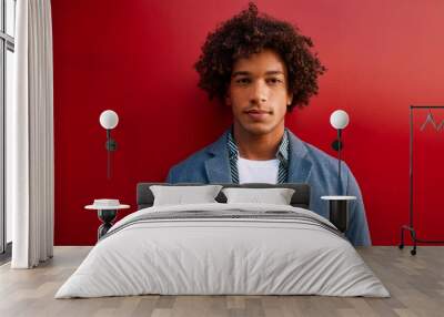 Portrait of a stylish man with curly hair posing in front of a vibrant red wall with a confident expression for a fashion editorial shoot Wall mural