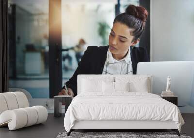 Success is a consistent, daily effort. Shot of a young businesswoman making notes at her desk in a modern office. Wall mural