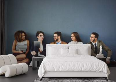 The connected team has great rapport. Studio shot of a group of businesspeople using wireless technology and talking on the floor against a gray background. Wall mural