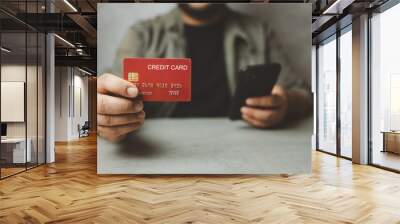 Man shows a red credit card and holding his phone. Shopping online by credit card with online service. Concept of paying for online shopping. Wall mural