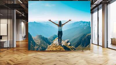 A woman feeling openness on a mountain peak with her arms outstretched. Wall mural