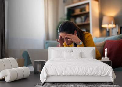 A pensive Caucasian woman in casual attire focuses on her laptop screen, displaying signs of worry as she sits on a cozy sofa in a well-lit living room. Wall mural