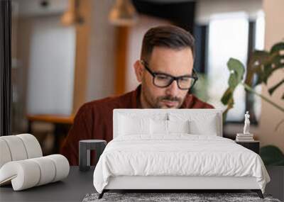 Front view of serious millennial man using laptop sitting at the working places, focused guy communicating online, writing emails, distantly working or studying on computer. Wall mural