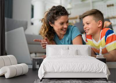 Portrait of cheerful mother pointing finger at laptop while lying on the floor with her son. Wall mural