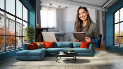 Smiling confident businesswoman looking at camera sitting at home office desk. Modern stylish female manager, successful female entrepreneur holding digital tablet posing for business portrait.. Wall mural