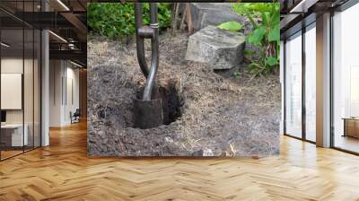 Steel post hole digger with metal shovel-like blades is being used to create a deep hole for a fence post with concrete bricks and green plants in the background. Wall mural