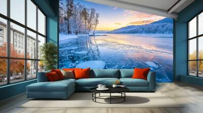 A breathtaking view of a frozen lake in a snow-covered forest, the sunset casting an orange glow over the icy surface. Trees on the bank are outlined in frost, with broken ice shards floating Wall mural