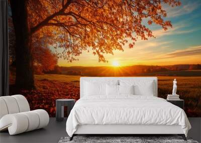 A serene autumn sunset illuminates a golden field with vibrant orange and red leaves under a large tree. Wall mural