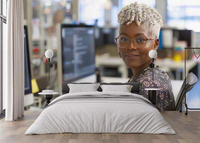 Confident African-American woman with glasses in a modern office setting, featuring a bright smile, stylish silver hair, and elegant floral patterned blouse, surrounded by blurred computer screens Wall mural