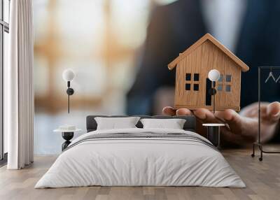 young man in suit holds wooden house model, symbolizing real estate and home ownership. His confident demeanor conveys professionalism and trust in real estate market Wall mural