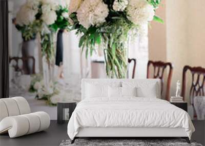 A pretty table decorated with two tall vases with a white and green flower arrangement centerpiece.  Wall mural