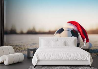 Close up of soccer ball with santa hat in on a field covered with snow. A sunny day at the football field. Wall mural