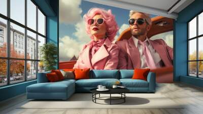 Man and woman on roof of car, man wears pink suit and pink tie and woman wears pink leather jacket and pink glasses, old pink car, cloudy blue than above Wall mural