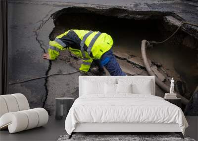 Road construction worker investigating Huge sinkhole on busy asphalt road surface on which cars drive. Accident situation on a city street due to cracks in asphalt. Broken hole filled with muddy water Wall mural