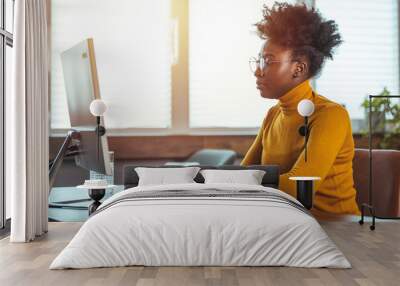 A focused mid adult Black businesswoman types intently at her desk in a sunlit home office, surrounded by modern technology and a cozy ambiance. Wall mural